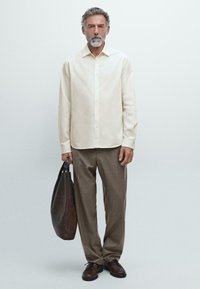 Camicia a maniche lunghe beige chiaro, con bottoni davanti, abbinata a pantaloni color sabbia. Scarpe in pelle marrone e una borsa tote in pelle texturizzata marrone scuro.