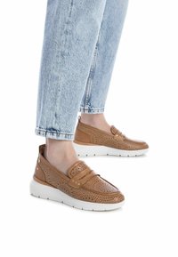 Scarpe in pelle perforata color beige con punta rotonda e dettagli a doppia fascia, dotate di una spessa suola bianca, indossate con jeans cropped azzurri chiari.
