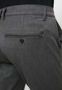 Grijze gestructureerde broek met een subtiele textuur, voorzien van een achterzak en een knoopsluiting. De tailleband is plat met ceintuurlussen.