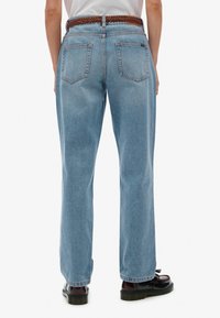 Vaqueros de mezclilla azul claro con diseño de pierna recta, que presentan cinco bolsillos y un cinturón trenzado marrón. Tejido texturizado con costuras visibles.