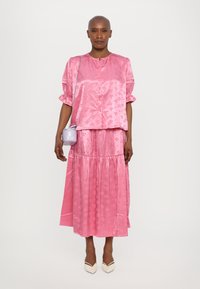 Rosa satengbluse med korte ermer og rund hals, sammen med et matchende langt skjørt; har blomsterdesign og lagdelt utforming.