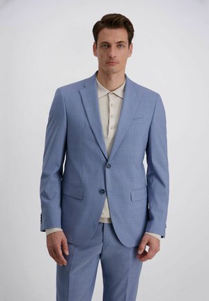 Mann trägt hellblauen Anzug mit Zweiknopfsakko und passenden Hosen, steht vor weißem Hintergrund.