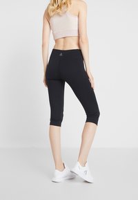 Zwarte capri leggings gemaakt van rekbaar materiaal, met een hoge tailleband en subtiele details. Gecombineerd met witte sportschoenen.
