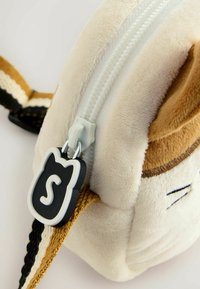 Plüschkatze-förmiger Beutel in Creme-, Braun- und Schwarztönen. Mit einem weißen Reißverschluss und einem schwarzen Reißverschlussanhänger in Katzenform mit einem 'S'-Akzent.