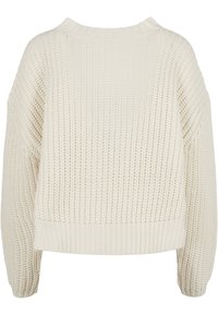 Pull en tricot couleur crème avec un motif de côtes texturé, encolure large à ras du cou et épaules tombantes. L'ourlet est légèrement court.