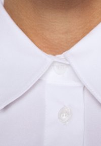 Camicetta bianca con colletto, realizzata in un tessuto liscio, con bottoni visibili al collo e un design del colletto pulito e strutturato.