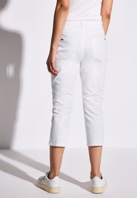 Witte verkorte broek gemaakt van katoen met twee achterzakken en een iets taps toelopende pijp, gecombineerd met witte sneakers op een effen achtergrond.
