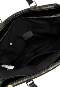 Interno di una borsa in pelle nera con rivestimento in tessuto liscio, dotata di una tasca con zip e un'etichetta impressa. Hardware della zip in oro visibile.
