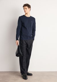 Camisa de manga larga azul marino con cuello redondo, combinada con pantalones negros y bolso negro. Tejido suave, marca mínima y silueta casual.