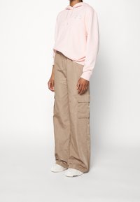 Ljusrosa huvtröja med framficka, kombinerad med beiga cargobyxor med sidfickor och lös passform. Vita sneakers fullbordar outfiten.