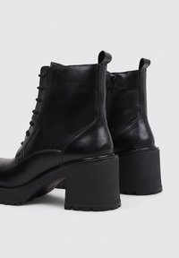 Bottes chelsea en cuir noir avec une finition texturée, un système de laçage à l'avant, une fermeture éclair à l'arrière et des talons en caoutchouc épais.