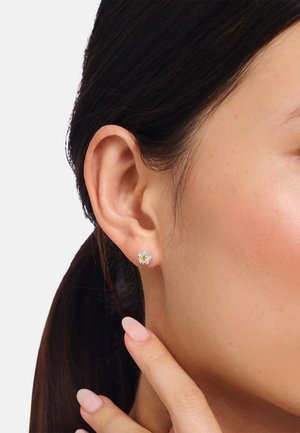 Gold- und silberne Steckohrringe mit floralem Design, das einen zentralen gelben Stein zeigt, umgeben von klaren Steinen in einer polierten Fassung.