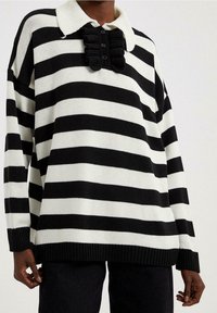 Sort-hvid stribet oversized strikket sweater med krave og knaplukning samt en flæsedetalje ved kraven.