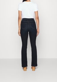 Jeans acampanados de un azul oscuro con una cintura alta, bolsillos traseros y detalles de costura mínimos, combinados con una camiseta blanca lisa.
