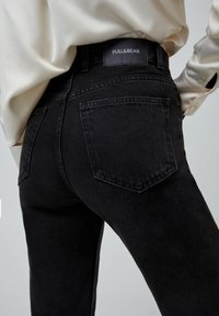 Jeans de denim negro con cintura alta, que presentan una etiqueta de Pull&Bear, dos bolsillos traseros y un acabado suave y texturizado.