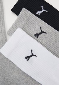 Drei Paar Socken in Schwarz, Grau und Weiß. Jede hat ein geripptes Design mit einem kleinen schwarzen Logo am Bündchen. Weicher Materialcharakter.