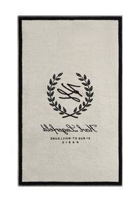 Taisnstūra paklājs krēmkrāsā ar melnu malu. Tam ir izšūta lauru dizaina un uzraksts: "YSL 31 Rue St. Guillaumme Parīze." Mīksta tekstūra.