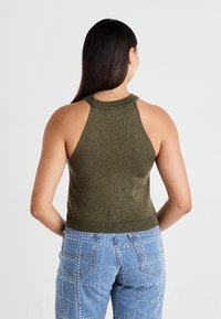 Top corto senza maniche di colore verde oliva con un collo alto, rifiniture a coste e una silhouette aderente, abbinato a jeans azzurri chiari decorati con borchie.