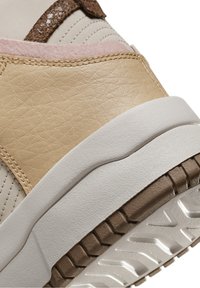 Béžové syntetické tenisky s texturovaným povrchem, s růžovými a hnědými akcenty. Silná bílá a hnědá gumová podešev s dezénem.