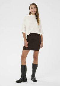 Top alb, cu maneci scurte; fustă mini din material maro, ajustată; cizme negre din piele, până la genunchi, cu fermoare și finisaj texturat. Design simplu, modern.