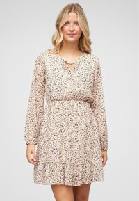 Robe à imprimé floral en rose clair, avec des manches longues, un col à nouer et un ourlet volanté. Fabriquée en tissu doux et léger.