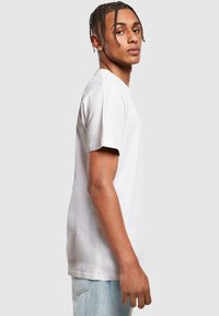 T-shirt en coton blanc avec un col rond et des manches courtes, présentant une coupe détendue et un ourlet droit, assorti à un jean bleu clair.