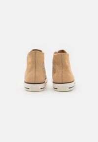 Sneakers înalte din suede bej, cu talpă din cauciuc albă, accente cu dungi negre și logo embosat pe tocul pantofului. Textură netedă, design minimalist.