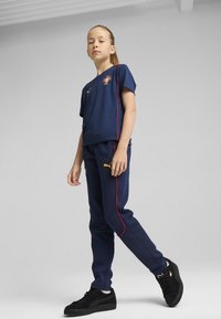 Mornarska sportska odjeća koja se sastoji od prilagođene majice s kratkim rukavima i suženih hlača s crvenim i zelenim bočnim trakama; uparen s crnim tenisicama.