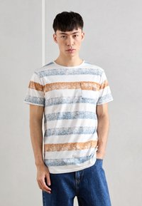 Camiseta de rayas en blanco, con texturas azules y naranjas en franjas horizontales, mangas cortas, cuello redondo y un bolsillo parche.