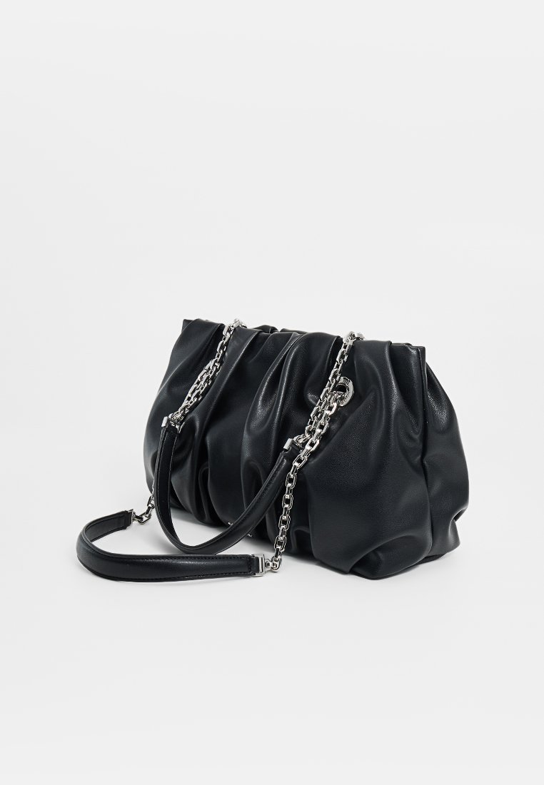 Bolso de cuero negro fruncido con cadena de plata y correa de cuero descansando sobre una superficie blanca.