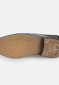 Zapato negro con un cuero liso en la parte superior y una suela de goma texturizada de color marrón claro. La talla 37 está marcada en la suela.