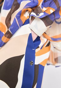 Multicolored blouse with abstract patterns in blue, orange, brown, and cream. Features a button closure and flowing, lightweight fabric.
