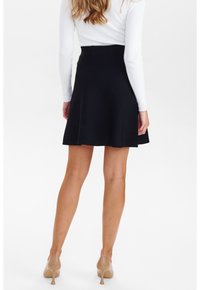 Jupe évasée noire à texture lisse, dotée d'une taille ajustée et de coutures latérales discrètes, associée à des chaussures à talons hauts couleur nude.