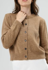 Bruine, gestructureerde cardigan met een ronde hals, lange mouwen en zeven zwarte knopen aan de voorkant. Geribbelde uiteinden aan de mouwen en zoom.