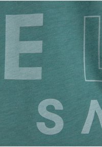 Teal cotton t-shirt featuring large white graphic text. The fabric has a smooth texture, with a relaxed, casual shape.