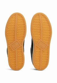 Czarne podeszwy sneakerów mają teksturowany, w formie plastra miodu, wzór z jaskrawą pomarańczową podeszwą. Branding "TOMMY JEANS" jest wyraźnie widoczny.