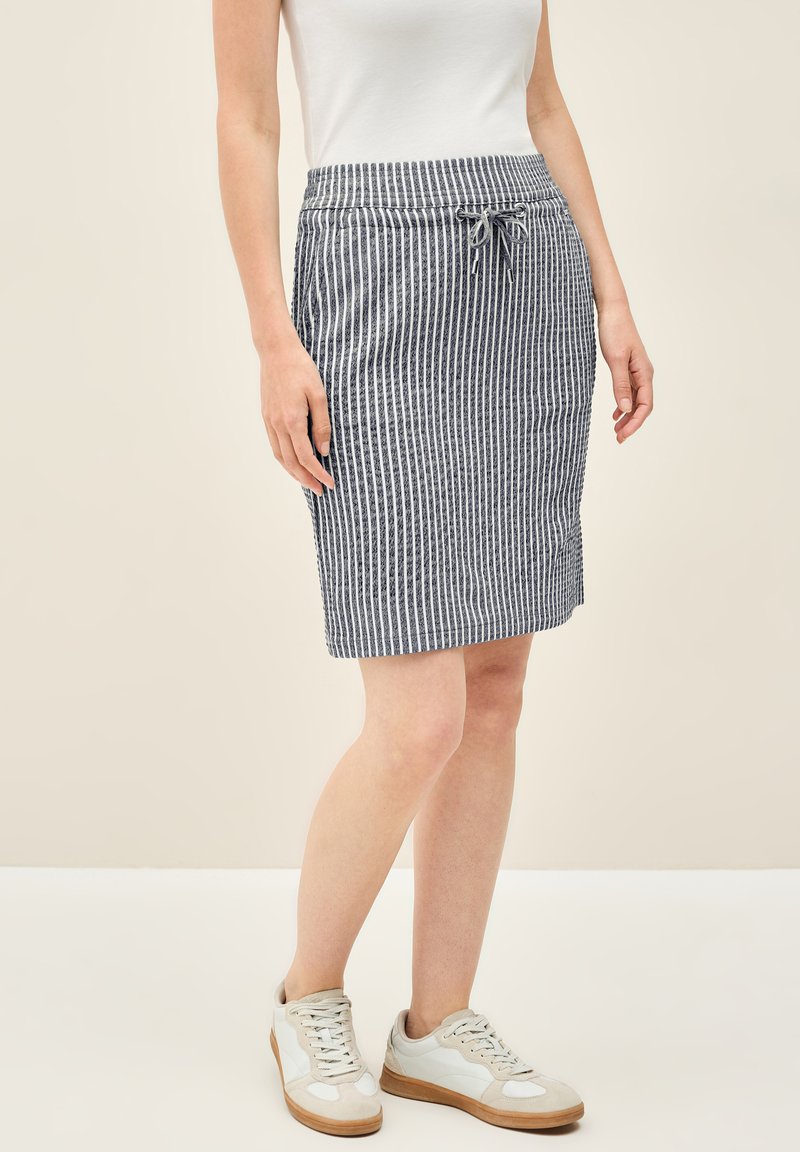 Gestreepte blauw-witte knielange rok met elastische taille en koord, gemaakt van een lichte stof, gecombineerd met witte sneakers.