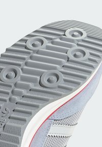 Gray rubber shoe sole with a textured surface, featuring grooves and circular patterns. Accented with a red trim and light gray suede details.