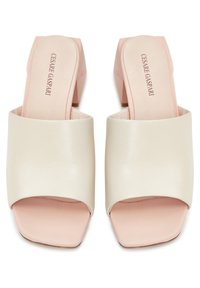 Paire de mules à talon bloc beige à bout ouvert avec larges brides en cuir et semelles intérieures roses de forme carrée sur fond blanc.