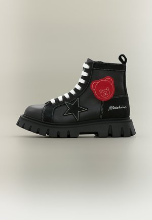 Czarny but taktyczny z białymi sznurówkami, czarną naszywką w kształcie gwiazdy, czerwoną naszywką z misiem, białym przeszyciem i logo Moschino po boku.