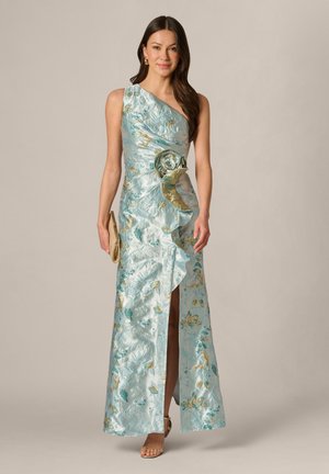 Vrouw draagt een mouwloze, lichtblauwe bloemenjurk met één schouder, ruches en een hoge split tot aan de dij, en houdt een gouden clutch vast.