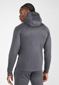 Grijze rits-hoodie met een gladde textuur, een aansluitend ontwerp en een capuchon. Voorzien van zijzakken en contrasterende stiksel langs de naden.