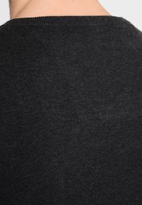 Un pull en tricot noir avec une texture lisse, un col rond et un léger éclat. Le tissu semble doux et flexible.