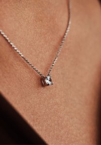 Collier en argent avec un pendentif en pierre précieuse transparente serti sur griffe, mettant en valeur un design délicat et une texture lisse sur la peau.