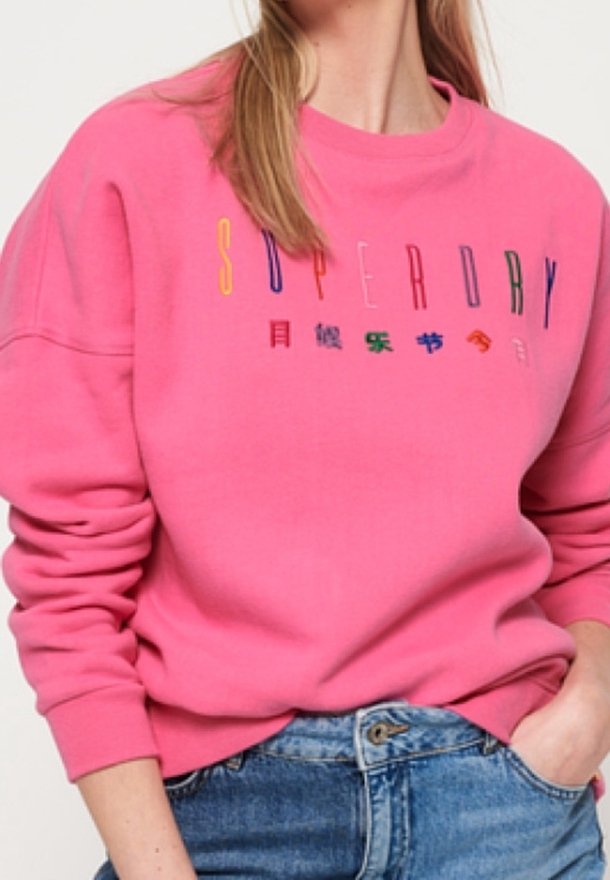 Pink sweatshirt with long sleeves, featuring a multicolored "SUPERDRY" logo across the chest, made from soft, textured fabric.