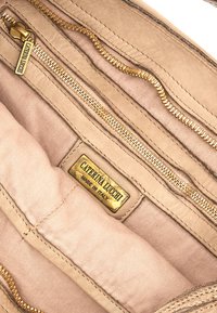 Interno di una borsa in pelle beige con cerniere dorate, dotato di molteplici scomparti e un'etichetta in ottone con la scritta "Caterina Lucchi, Made in Italy."