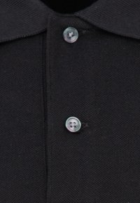 Czarny polo z klasycznym kołnierzykiem i zapięciem na guziki w kontrastowym jasnym kolorze, wykonany z gładkiego, teksturowanego materiału.