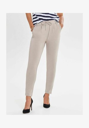 Beige Jogginghosen mit einem Kordelzugbund, schmalem Bein, glatter Textur und Seitentaschen, kombiniert mit schwarzen hohen Schuhen.