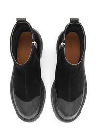 Botas negras hasta el tobillo de ante con detalles de goma. Presentan una suela texturizada y un detalle de cremallera en el lateral. Forro interior suave.