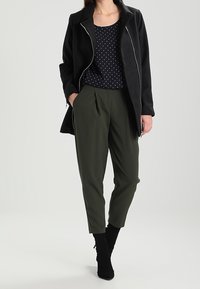 Černá zipová bunda, námořnická modrá tank top s puntíky, olivově zelené zúžené kalhoty a černé kotníkové boty. Hladká látka s přizpůsobeným střihem.